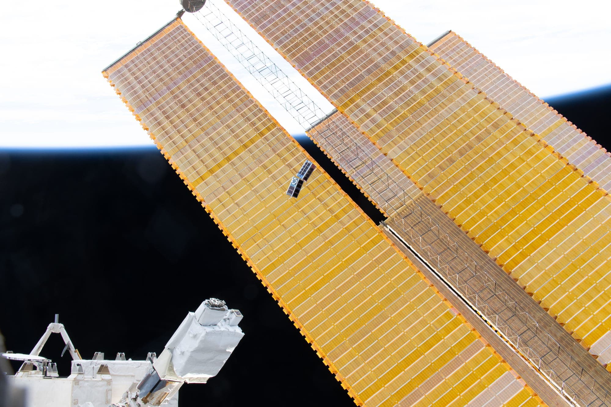 A small CubeSat drifting away from the International Space Station past its solar arrays