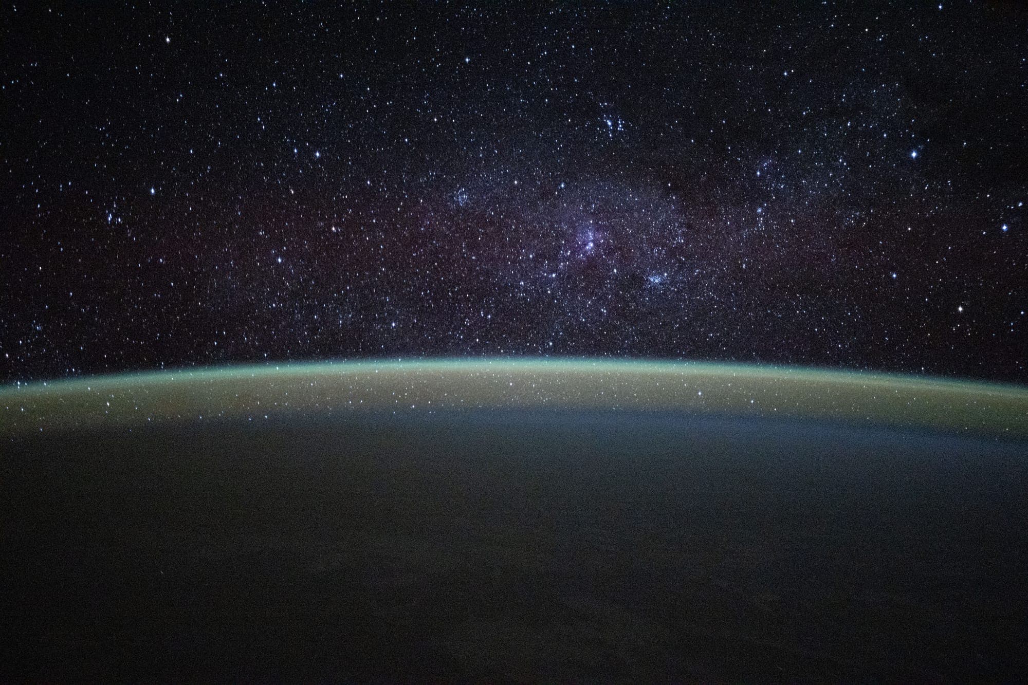 Stars above the faint green glow of the upper atmosphere, seen from orbit